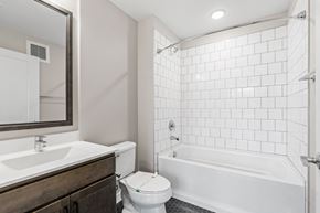 Minneapolis apartment for rent - A modern bathroom with a dark wood vanity, white sink, toilet, and a bathtub with white subway tile walls.