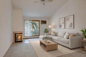Plymouth apartment for rent - A cozy living room here at Plymouth Square featuring a neutral color palette with a plush sectional sofa, soft area rug, and a light wood coffee table accented by simple décor. A corner fireplace adds warmth, while sliding glass doors open to a private balcony that brings in natural light and leafy outdoor views.