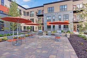 St. Louis Park apartment for rent - A patio with tables and chairs and umbrellas in front of apartment buildings.