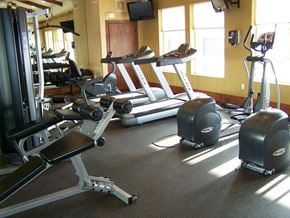 Plymouth apartment for rent - A well-equipped fitness center here at Stoneleigh at the Reserve featuring treadmills, elliptical machines, and strength-training equipment arranged on rubber flooring, with large windows bringing in natural light, wall-mounted televisions, mirrors, and warm neutral walls creating a bright and functional workout space.
