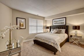 Minneapolis apartment for rent - A serene bedroom here at The Fairway featuring a spacious layout with soft neutral carpeting, a plush bed with patterned bedding and layered pillows, matching bedside tables with decorative lamps, framed wall art, a large window with blinds that allows natural light, and a sleek desk area that adds both comfort and functionality.