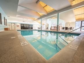 Eagan apartment for rent - A sunny outdoor swimming pool here at Town Centre featuring a rectangular pool with clear blue water, stainless handrails, and a spacious concrete deck lined with lounge chairs, set against a backdrop of mature trees, open sky, and perimeter fencing that creates a relaxing space for warm-weather recreation.
