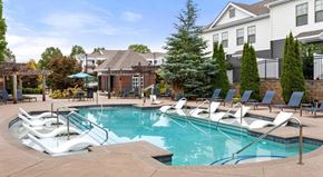 Charlotte apartment for rent - A resort-style pool here at CityPark View featuring in-water lounge chairs, wide steps with handrails, and a spacious pool deck lined with chaise seating. A pergola-covered area and umbrella tables provide shaded spots, while landscaped greenery and surrounding residential buildings create a relaxed, community-focused outdoor setting.