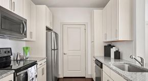 Charlotte apartment for rent - A sleek galley-style kitchen here at CityPark View featuring light wood cabinets, speckled countertops, and a stainless-steel refrigerator, stove, microwave, sink, and dishwasher. Upper and lower cabinetry provides ample storage, while clean lines, modern fixtures, and bright lighting create a fresh, contemporary feel.
