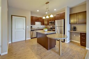 Williston apartment for rent - A modern, open kitchen here at Dakota Commons featuring rich wood cabinetry, stainless steel appliances, a spacious center island with an extended breakfast bar, warm wood-style flooring, and pendant lighting that creates a bright, functional space ideal for cooking and entertaining.