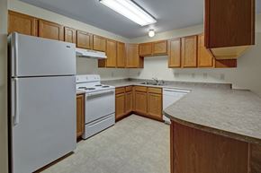 Stanley apartment for rent - A bright, functional kitchen here at Dakota featuring warm wood cabinetry, white appliances including a refrigerator, stove, and dishwasher, durable neutral countertops, vinyl flooring, and ample counter space that creates a clean and practical apartment cooking area.