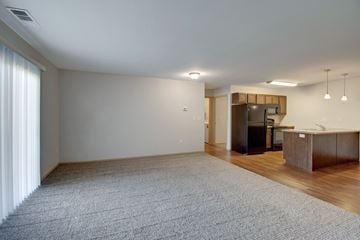 Watford City apartment for rent - A spacious living room with a grey carpet and a kitchen area in the background.