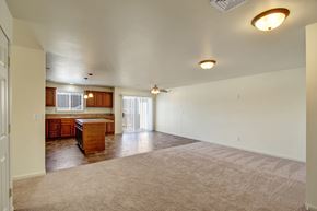 Williston apartment for rent - A spacious open living area here at Phoenix Ridge featuring soft neutral carpeting, an open-concept layout flowing into a kitchen with warm wood cabinetry, a center island, tile flooring, pendant lighting, and a sliding glass door that brings in natural light and connects to an outdoor space.