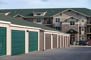 Williston apartment for rent - A convenient detached garage area here at Prairie Pines at the Ridge featuring rows of private garage doors with paved drive lanes, set in front of a multi-story apartment building with stone accents, neutral siding, and a well-maintained residential community layout.
