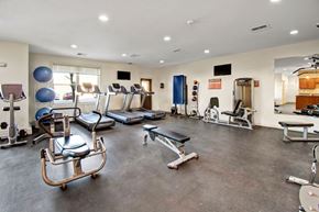 Williston apartment for rent - A spacious community fitness center here at Prairie Pines at the Ridge featuring treadmills, strength training machines, free weights, exercise balls, wall-mounted TVs, and durable flooring in a bright, open layout designed for convenient and comfortable workouts.