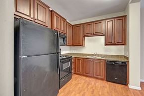 Williston apartment for rent - A bright kitchen here at Prairie Vista showcasing rich wood cabinetry, black appliances, granite-style countertops, wood-look flooring, and a functional L-shaped layout that offers ample storage and counter space for everyday cooking and entertaining.