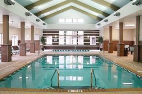 Williston apartment for rent - A bright indoor swimming pool here at Renaissance Heights featuring clear turquoise water, stainless steel handrails, a vaulted ceiling with exposed beams, large windows letting in natural light, tiled pool decking, and surrounding seating areas that create a relaxing, resort-style atmosphere.