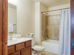 Williston apartment for rent - A clean, inviting bathroom here at Rockridge Apartments with a bathtub and tiled shower surround, a white toilet, and a wooden vanity with a white countertop. A large wall mirror hangs above the sink, and neutral wall colors with simple finishes create a bright, well-maintained space.