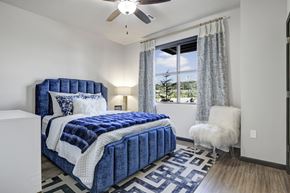 Tulsa apartment for rent - A bright bedroom here at 71 at Tulsa Hills with wood-style flooring, a plush blue upholstered bed, soft neutral bedding, and a window dressed with light curtains that allows natural light to fill the space for a calm, inviting feel.