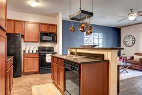 Oklahoma City apartment for rent - A functional kitchen here at Aviare Arts District with warm wood cabinetry, black appliances, wood-style flooring, and a breakfast bar with pendant lighting, opening into the living area for a comfortable and practical layout.