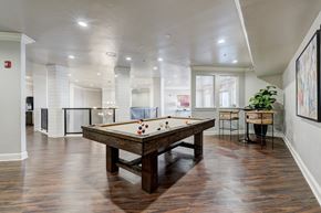 Oklahoma City apartment for rent - A spacious game room here at Aviare Arts District with a classic pool table, wood-style flooring, modern lighting, and bar-height seating, creating a bright and inviting space for residents to relax and socialize.