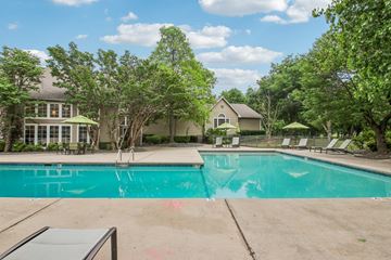 Oklahoma City apartment for rent - A swimming pool surrounded by trees and a house in the background.