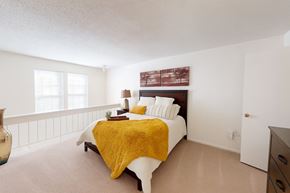 Oklahoma City apartment for rent - A bright bedroom here at Brookwood Village with beige carpet, soft neutral walls, and natural light from multiple windows, featuring a cozy bed with warm accent bedding and an open, airy layout that feels calm and inviting.