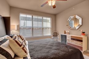 Tulsa apartment for rent - A bedroom with a bed, chair, and a mirror on the wall.
