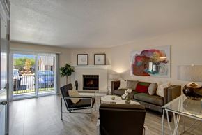 Oklahoma City apartment for rent - A cozy living room here at Indigo with wood-style flooring, neutral walls, and a fireplace with a mantle. A sliding glass door with vertical blinds brings in natural light and leads to a patio area, while comfortable seating and modern wall art create a warm, inviting atmosphere.
