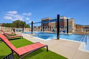 Oklahoma City apartment for rent - A resort-style pool here at Indigo with clear blue water, shaded lounge areas, and surrounding deck space. A nearby clubhouse and seating areas create a relaxing and inviting outdoor community space.