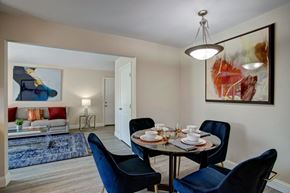 Oklahoma City apartment for rent - A modern dining area here at Indigo with a round dining table, upholstered chairs, and a contemporary hanging light fixture. A nearby living room with comfortable seating and modern wall art creates a warm, open, and inviting layout.