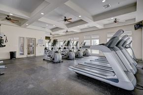 Oklahoma City apartment for rent - A fitness center here at Liberty Pointe featuring treadmills, stationary bikes, and elliptical machines arranged across an open workout floor. The space has bright recessed lighting, ceiling fans, and multiple windows that bring in natural light for a clean, energized atmosphere.