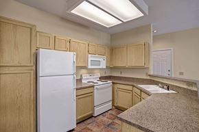 Tulsa apartment for rent - A bright kitchen here at Lincoln Villas on Memorial with light wood cabinets, speckled countertops, and white appliances. A double-basin sink and pass-through bar area create a functional, open layout with a clean, neutral feel.