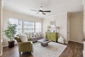 Oklahoma City apartment for rent - A living room here at Lincoln at Central Park featuring a bright, modern space with a light gray sofa, a green accent chair, and a green decorative dresser that adds a standout pop of color. Large windows with white curtains bring in natural light, while a light area rug, square coffee table, and indoor plant create a clean, comfortable feel.