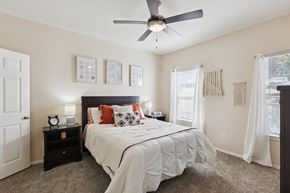 Oklahoma City apartment for rent - A bedroom here at Lincoln at Central Park featuring a dark wood bed frame styled with white bedding and standout rust-orange accent pillows and throw for a warm pop of color. Matching dark wood nightstands with modern lamps and décor sit on each side, while neutral wall art above the bed and soft white curtains over the windows keep the space bright, clean, and inviting.