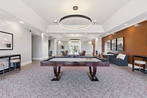 Oklahoma City apartment for rent - A modern resident lounge here at Lincoln at Central Park with plush carpet flooring, a pool table centerpiece, and stylish circular ceiling lighting. A warm accent wall, comfortable seating, and dining space create a welcoming, upscale social atmosphere.