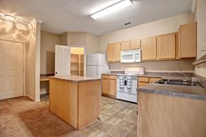 Tulsa apartment for rent - A kitchen here at Memorial Creek with light wood cabinets, a center island, neutral countertops, white appliances, tiled flooring, and an open layout connecting to the dining and living areas.A kitchen here at Memorial Creek with light wood cabinets, a center island, neutral countertops, white appliances, tiled flooring, and an open layout connecting to the dining and living areas.