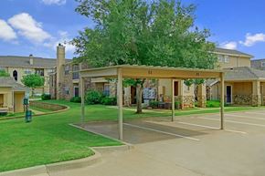 Oklahoma City apartment for rent - A covered parking area here at Quail Landing with carport spaces, green lawns, mature trees, and surrounding apartment buildings, offering a clean, convenient, and well-maintained community setting.