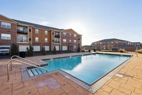 Oklahoma City apartment for rent - A large swimming pool surrounded by a brick walkway and a metal railing.