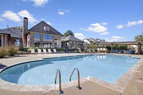 Oklahoma City apartment for rent - A resort-style swimming pool here at Stoneleigh on May with clear blue water, poolside lounge chairs, and surrounding greenery. A clubhouse backdrop and open sky create a relaxing, community-focused outdoor setting.
