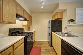 Oklahoma City apartment for rent - A functional kitchen here at Summit Point with warm wood cabinets, light countertops, and black appliances. Track lighting brightens the space, while wood-style flooring and a double sink create a cozy, practical cooking area.