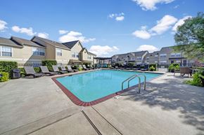 Oklahoma City apartment for rent - A swimming pool surrounded by a concrete patio and a row of houses.