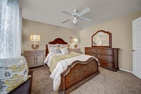 Oklahoma City apartment for rent - A spacious bedroom here at Summit Point with plush carpet, soft neutral walls, and a ceiling fan with light. A large bed with classic wood furniture and warm lighting creates a comfortable, inviting retreat.