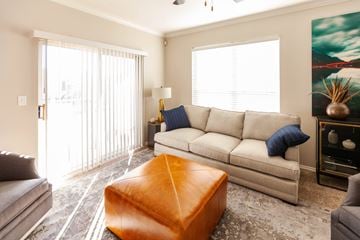 Oklahoma City apartment for rent - A living room with a grey couch, a brown ottoman, and a painting on the wall.
