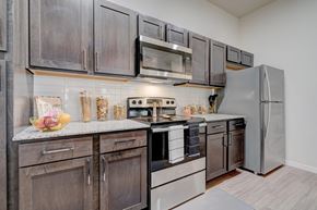 Oklahoma City apartment for rent - A modern kitchen here at The Encore with dark wood cabinets, granite-style countertops, and stainless steel appliances. A subway tile backsplash and clean finishes create a polished, contemporary cooking space.