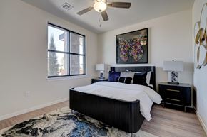 Oklahoma City apartment for rent - A bedroom here at The Encore with a black bed frame, crisp white bedding, and colorful wall art above the headboard. Light flooring, matching nightstands with lamps, a ceiling fan, and a large window create a bright, modern feel.
