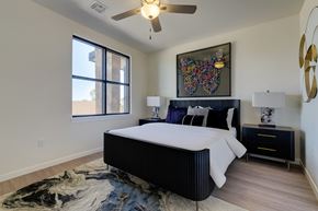 Yukon apartment for rent - A bedroom here at Trailwinds with a black bed frame, white bedding, dark nightstands, colorful butterfly wall art, ceiling fan, large window, and soft patterned rug creating a bright, modern feel.