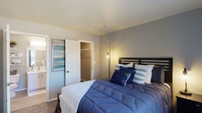 Moore apartment for rent - A bedroom here at Villas at Countryside with blue bedding on a black bed frame, soft gray walls, warm bedside lighting, and an open view into a bright bathroom and closet creating a calm, welcoming feel.
