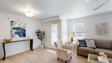 Owasso apartment for rent - A living room with a grey couch, a yellow bowl on a black table, a painting on the wall, a plant, a chair, and a coffee table.