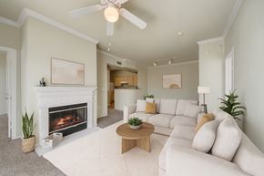 Broken Arrow apartment for rent - A living room here at Woodland Park with a light beige sofa set, cream rug, and round wood coffee table, centered around a white fireplace, with soft green walls, crown molding, and a white ceiling fan overhead.