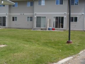 Fort St. John apartment for rent - A grassy area in front of a grey building with a red post in the foreground.