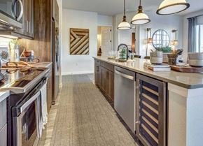 Cedar Park apartment for rent - A kitchen here at Alden at Cedar Park with dark wood cabinets, white island countertop, stainless appliances, pendant lights, built-in wine fridge, and a long runner rug along the floor.