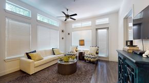 Dallas apartment for rent - A bright living room here at Arpeggio with tall windows, white sofa, blue and yellow accent chairs, dark wood floors, a round coffee table, ceiling fan, and a glass door bringing in natural light.