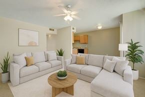 Midland apartment for rent - A bright, inviting living room here at Avalon Springs with light carpet and neutral walls, featuring plush cream-colored sofas, a round wooden coffee table, potted greenery, and a ceiling fan, with an open view into the kitchen that creates a comfortable, modern atmosphere.