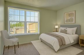 Midland apartment for rent - A calm, inviting bedroom here at Avalon Springs with soft neutral walls and plush carpet, featuring a comfortable bed with light bedding, a bedside lamp, and natural light filtering through a large window with vertical blinds for a bright and restful atmosphere.